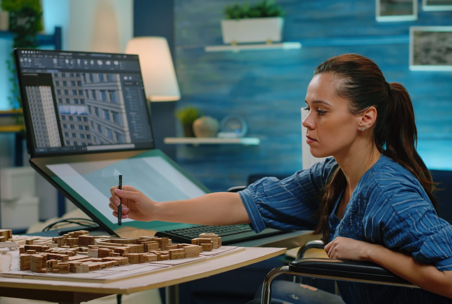 Invalid engineer looking at building model on computer designing layout and blueprint for construction. Architect in wheelchair using touch screen monitor to analyze architectural structure